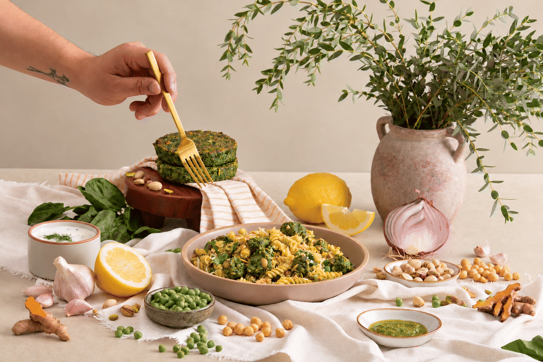 A fork reaches into spinach and pistachio patty pasta and lifts a bite.